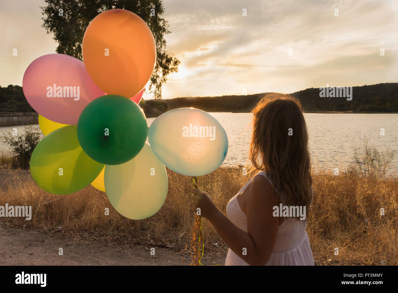Woman with colorful balloons watching the sunset, on a lake in Toledo, Spain Stock Photo