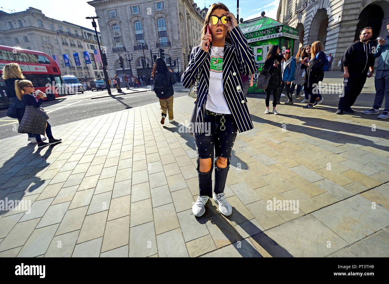 Fashionable young woman with ripped knee jeans on her mobile phone in  Piccadilly Circus, London, England, UK Stock Photo - Alamy