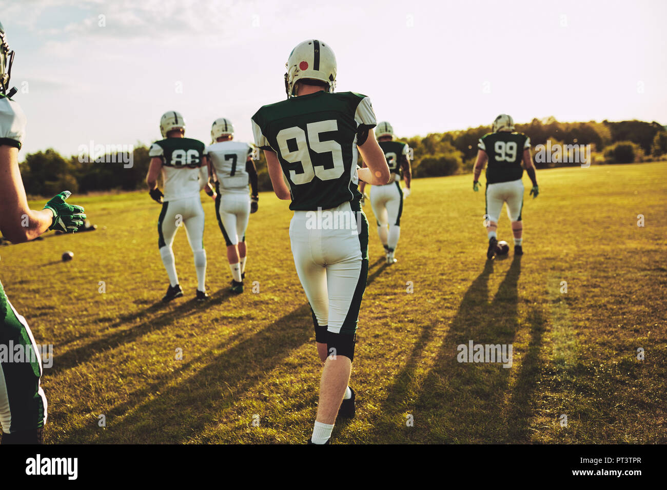 Rearview of a team of young American football players walking onto a sports field together for practice on a sunny afternoon Stock Photo
