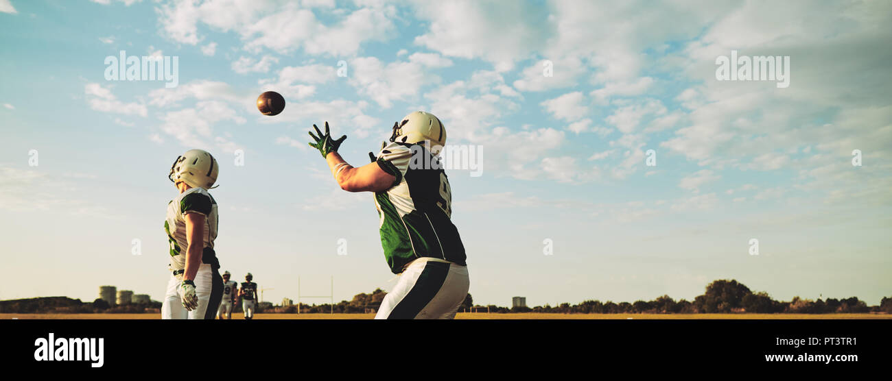 American football player receiving a pass during team practice drills on a football field in the afternoon Stock Photo