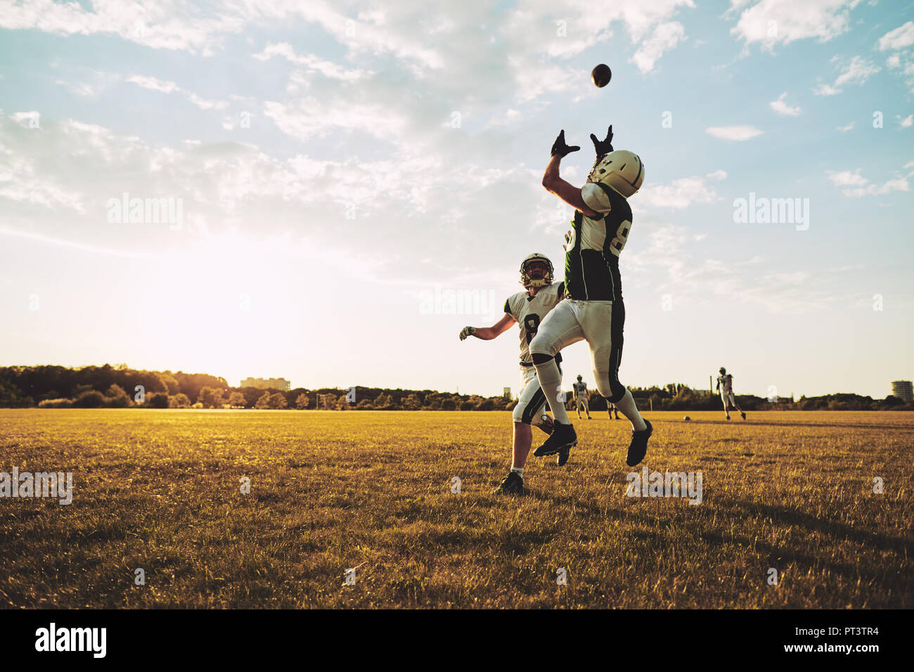 Young American football player receiving a pass during team practice on a football field in the afternoon Stock Photo