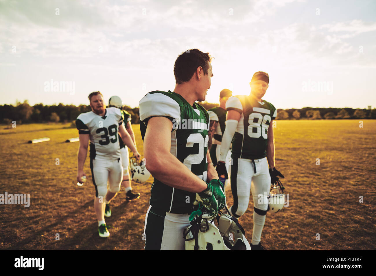 Team of smiling young American football players walking off a sports field together after an afternoon practice Stock Photo