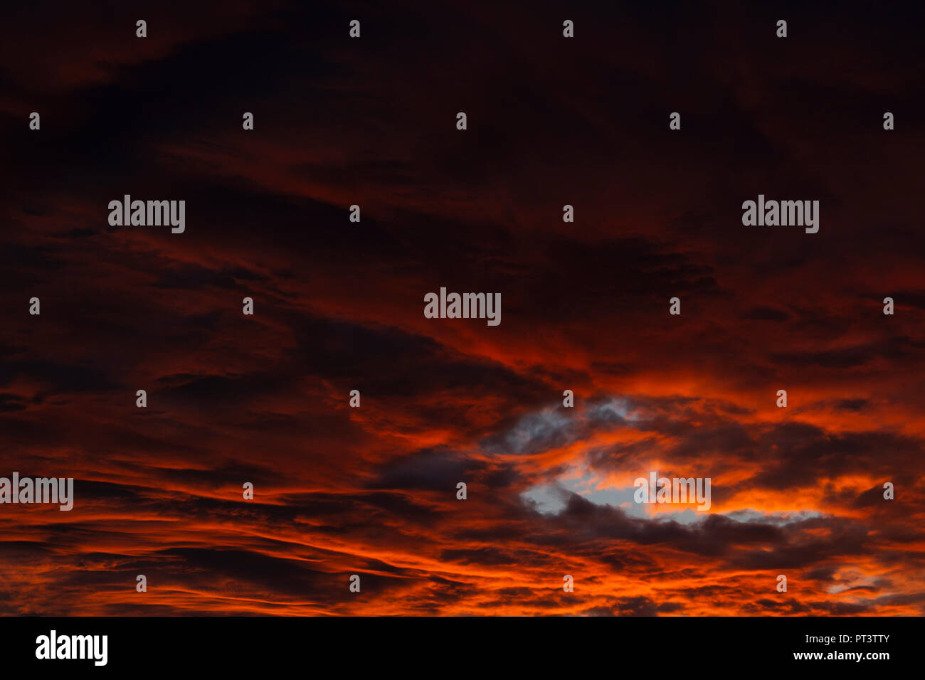 Clouds lit orange by sunset, gradient from darker to brighter. Cloud hole with blue sky. Stock Photo