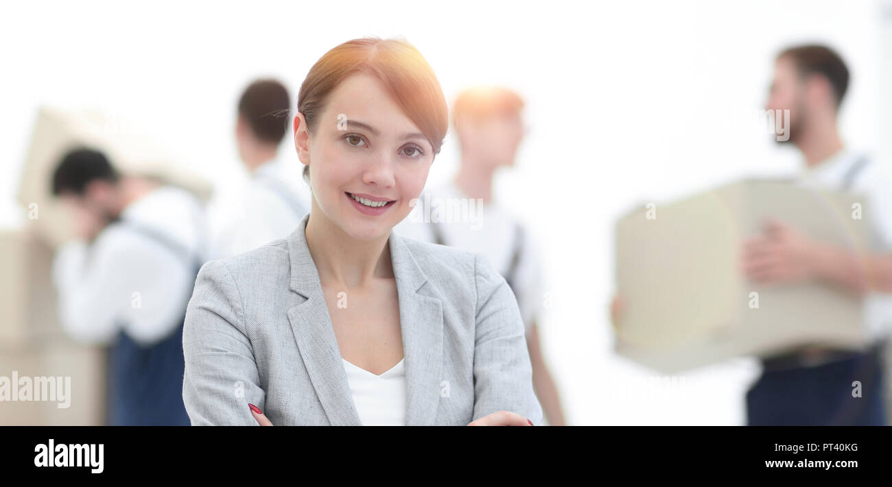 Smiling manager holding clipboard on blurred background with movers and boxes. Stock Photo