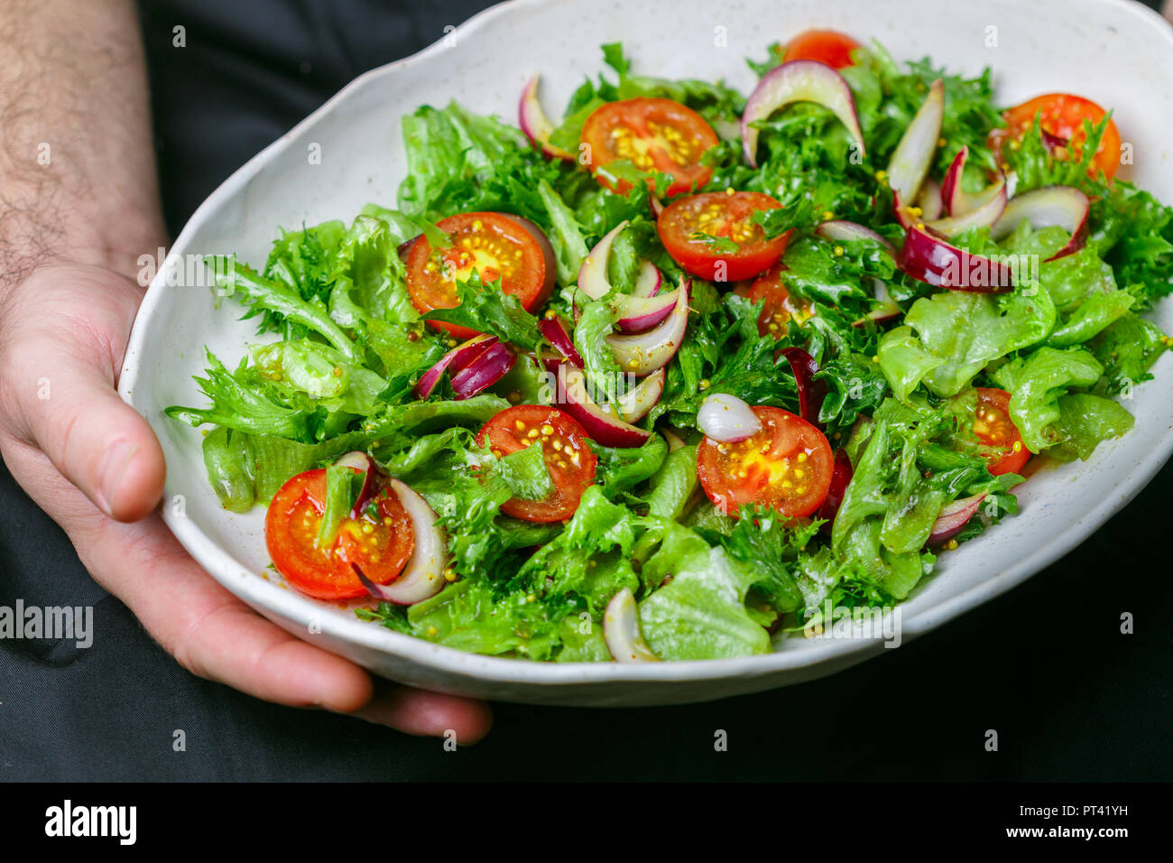 White plate with lettuce, cherry tomatoes and red onion salad with olive oil, mustard and wine