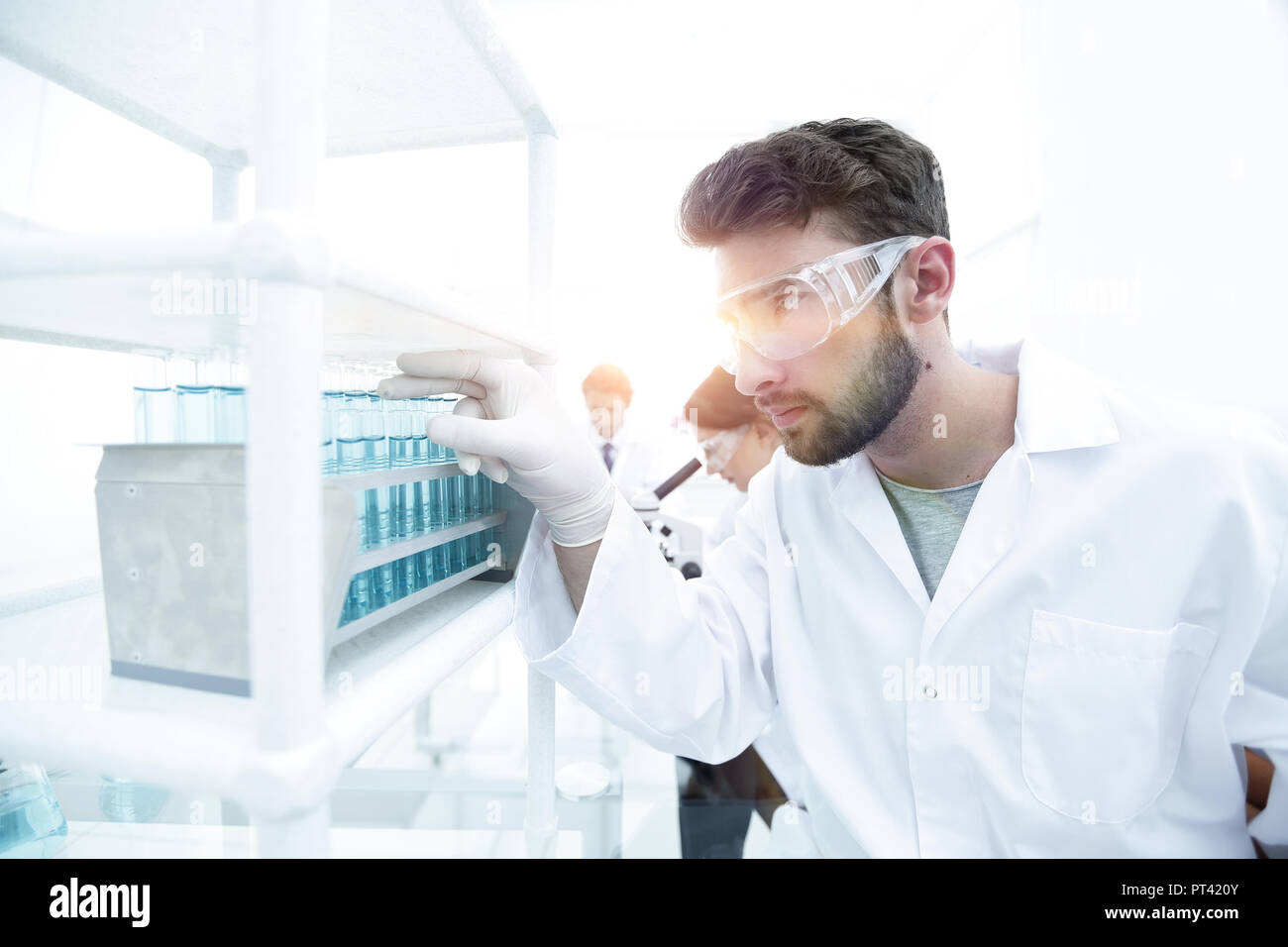 Side view of young scientist in eyeglasses looking at test tube in ...
