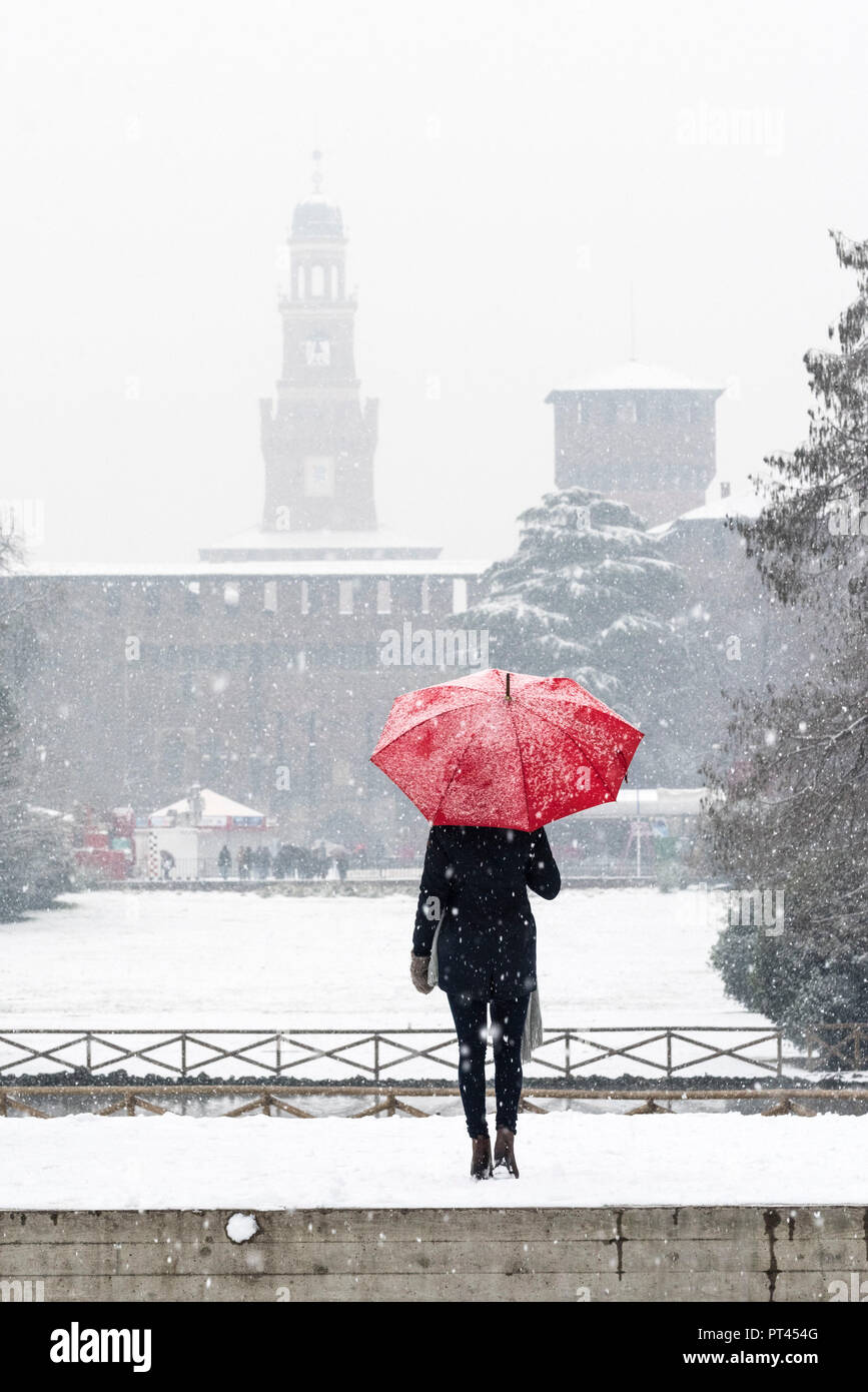 A woman with red umbrella admires the view of Sempione park during a snowfall, Milan, Lombardy, Italy, Europe, Stock Photo