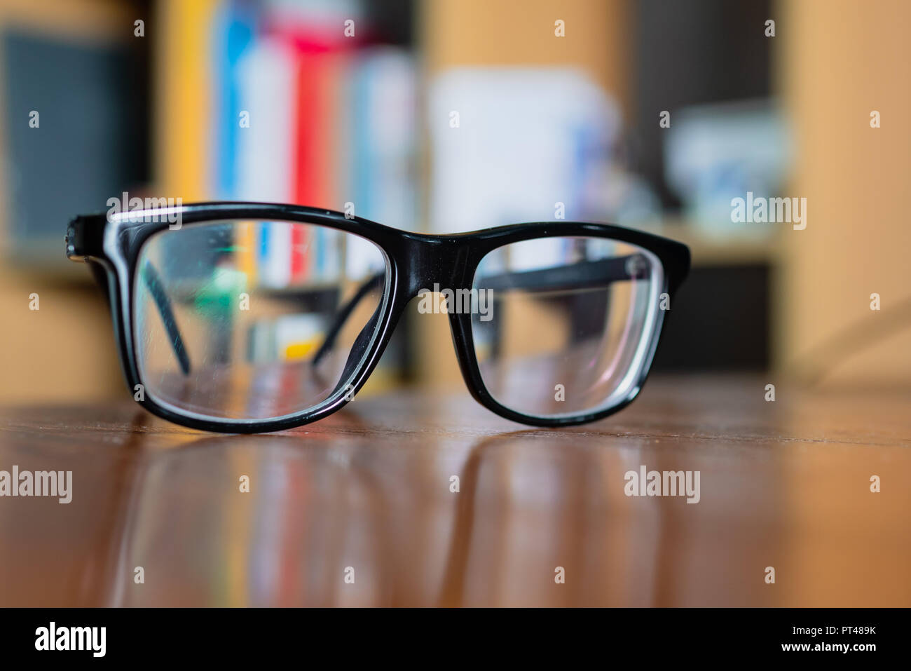 Eyeglasses on a table with bookshelf on background Stock Photo