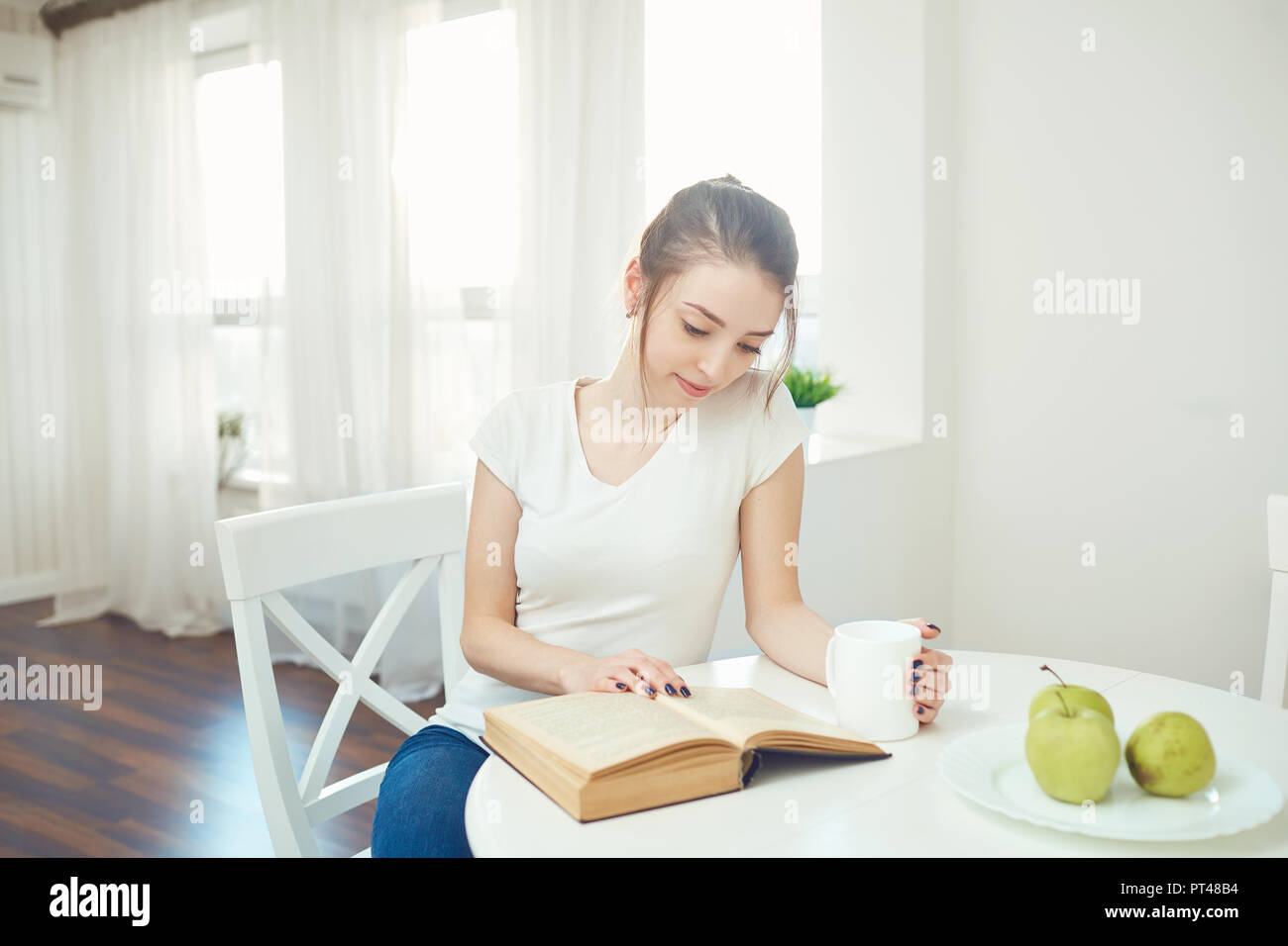 A young girl is reading a book sitting at a table. Stock Photo