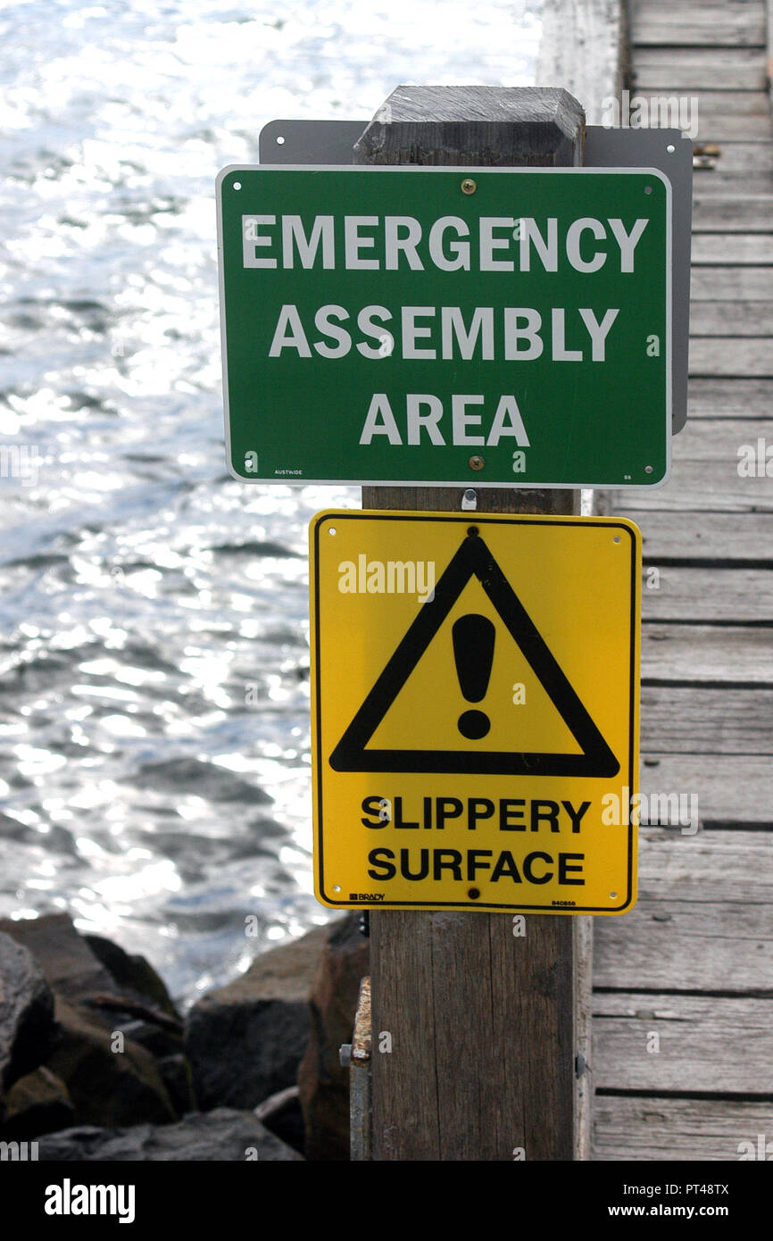 GREEN AND WHITE EMERGENCY ASSEMBLY POINT & YELLOW SLIPPER SURFACE SIGNS, COASTAL TASMANIA, AUSTRALIA. Stock Photo