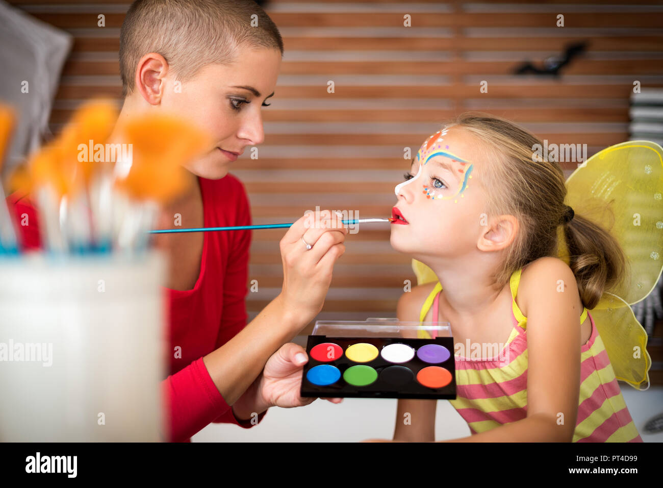 Young mother painting daughters face for Halloween party. Halloween or carnival family lifestyle background. Face painting and dressing up. Stock Photo