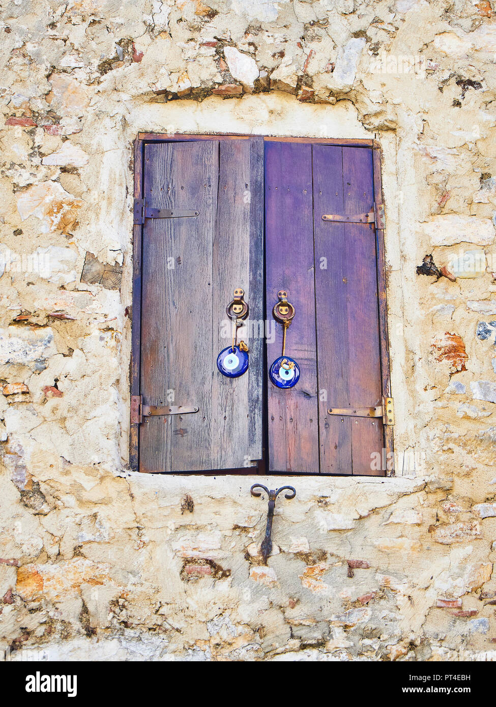 Antique wooden window on a stone wall with a Nazar boncugu, a Turkish eye-shaped amulet. Stock Photo
