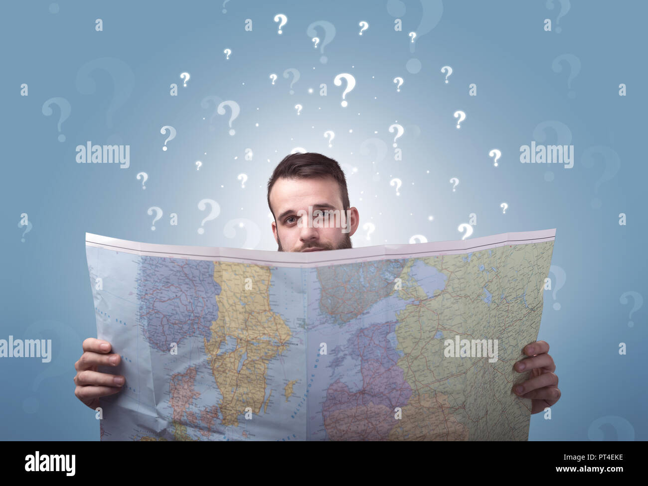 Handsome young man holding a map with white question marks above his ...