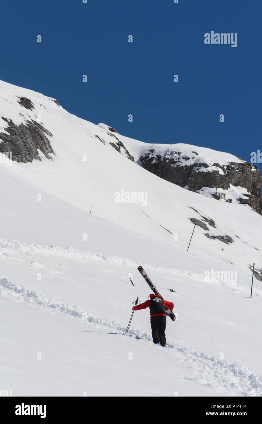 Ski patrol climbing up a mountain slope carrying large skis Stock Photo