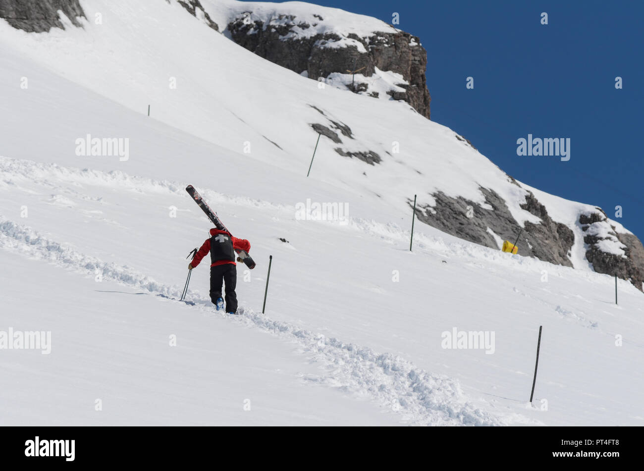 Ski patrol climbing up a mountain slope carrying large skis Stock Photo