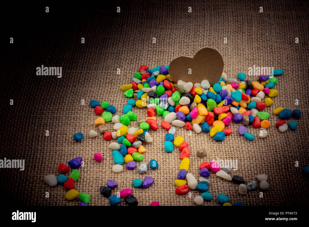 Paper heart amid colorful pebbles on canvas ground Stock Photo