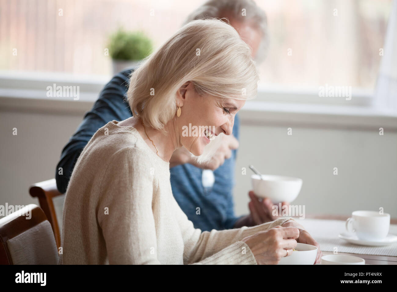 Happy grey haired woman having breakfast with aged husband at home, smiling beautiful old lady enjoys morning meal with mature man, senior family coup Stock Photo