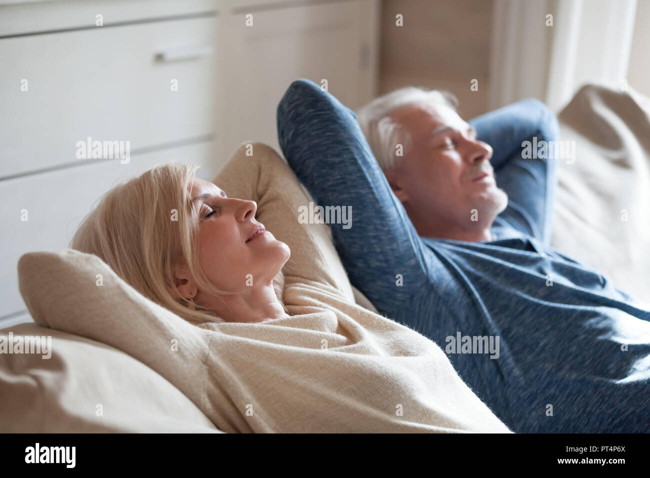 Calm senior mature couple relaxing on soft comfortable sofa having daytime nap together, carefree middle aged old family breathing fresh air enjoying  Stock Photo