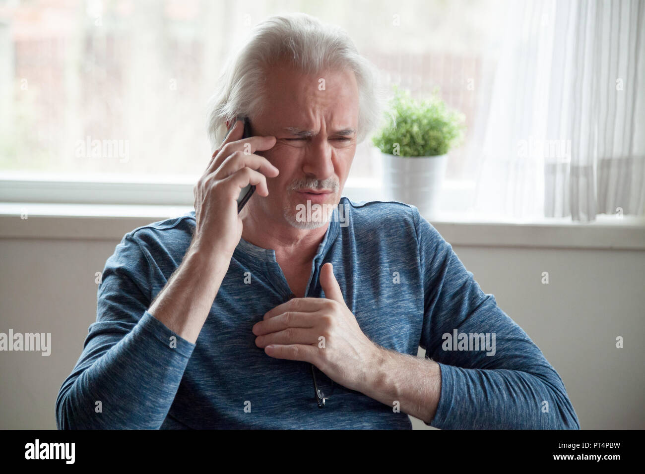 Stressed senior man having heart attack while talking on phone Stock Photo