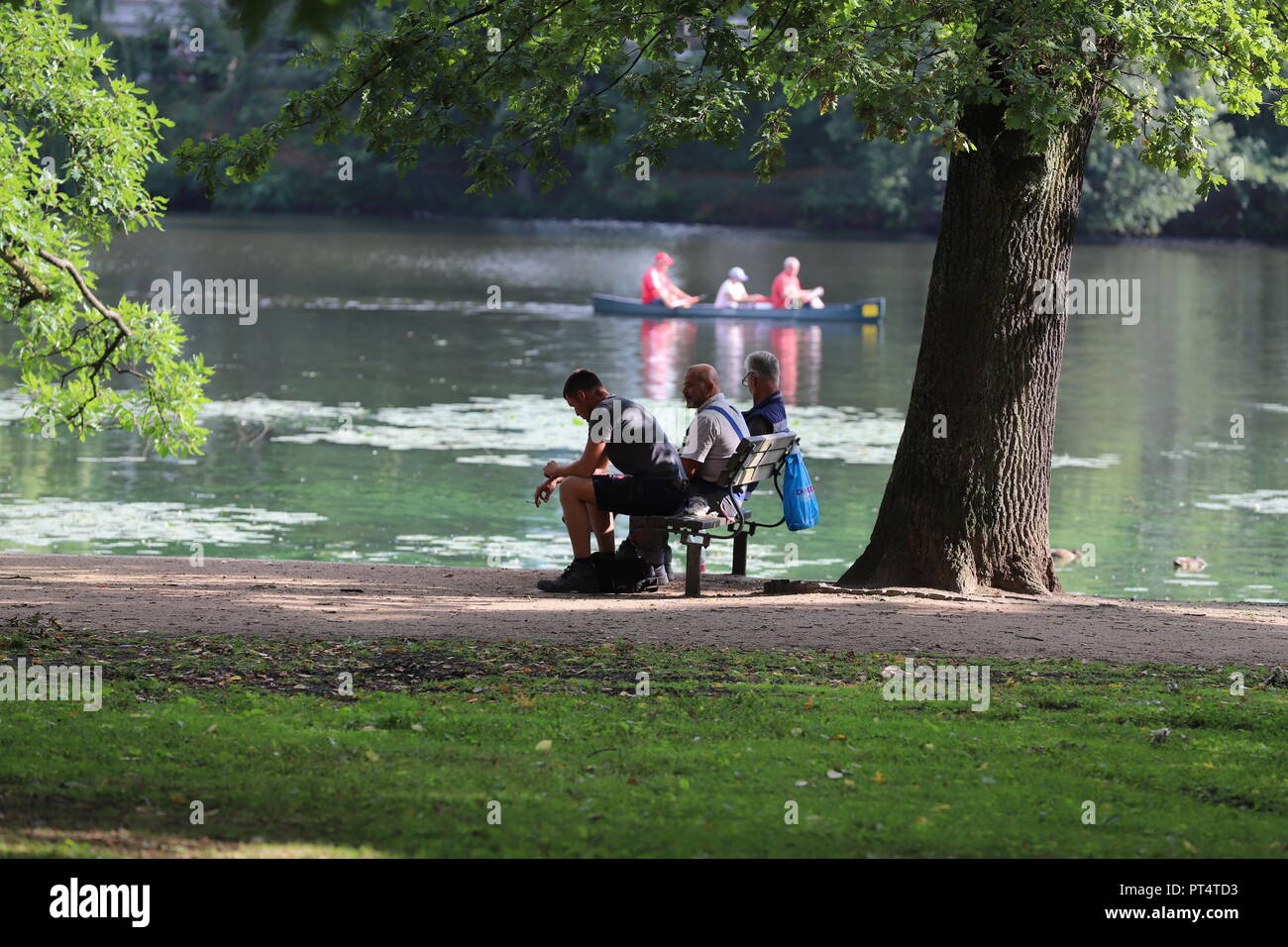 three people resting on a bench next to the Alster Stock Photo