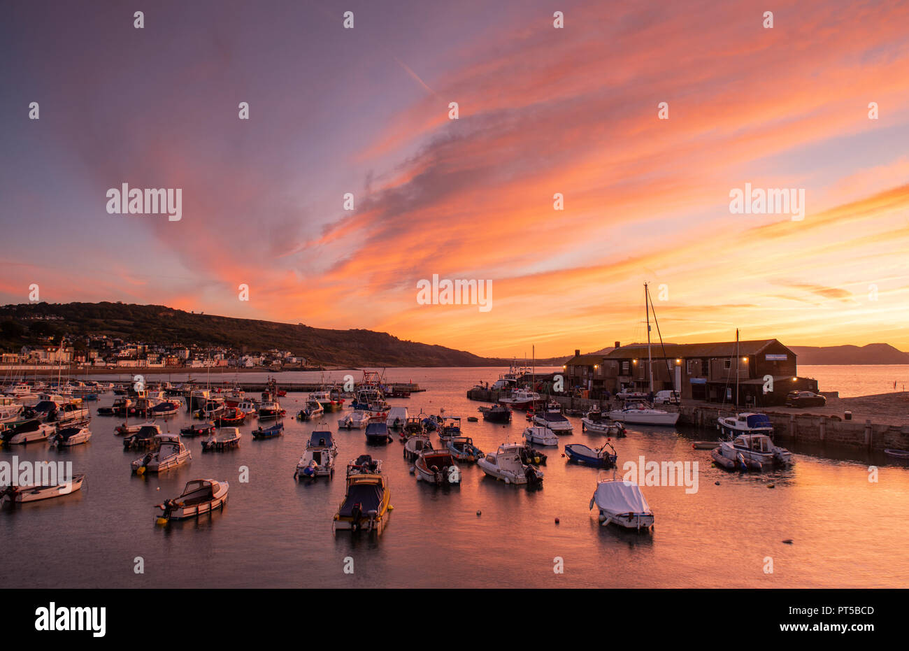 Lyme Regis, Dorset, UK. 7th October 2018.  UK Weather:  The skies over the Cobb Harbour glow with vibrant colour at the start of a bright and sunny autumn day at Lyme Regis.  Credit: Celia McMahon/Alamy Live News Stock Photo