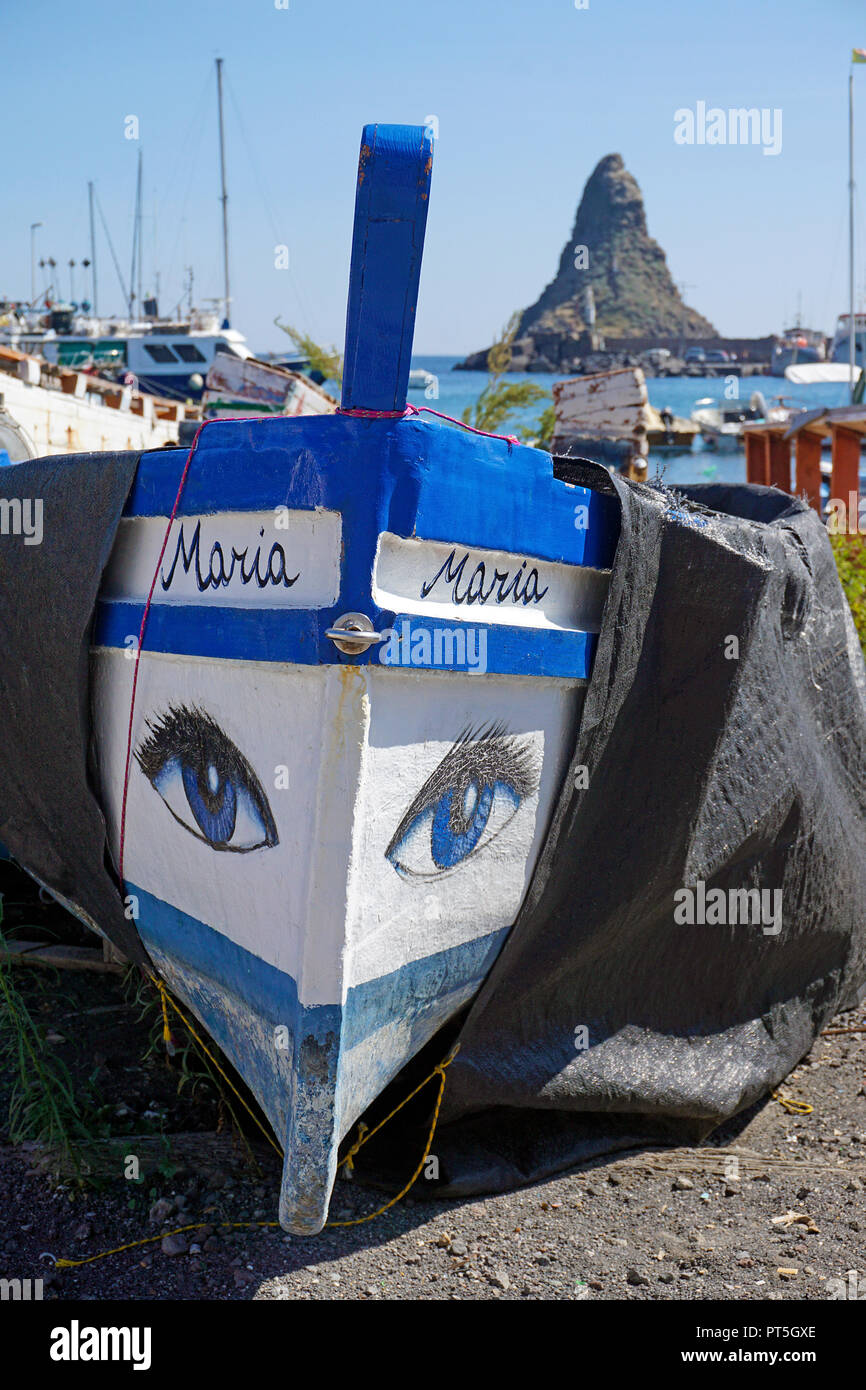 Fishing boat with painted eyes at harbour of Aci Trezza, behind the Faraglione grande, cyclops islands, comune of Aci Castello, Catania, Sicily, Italy Stock Photo