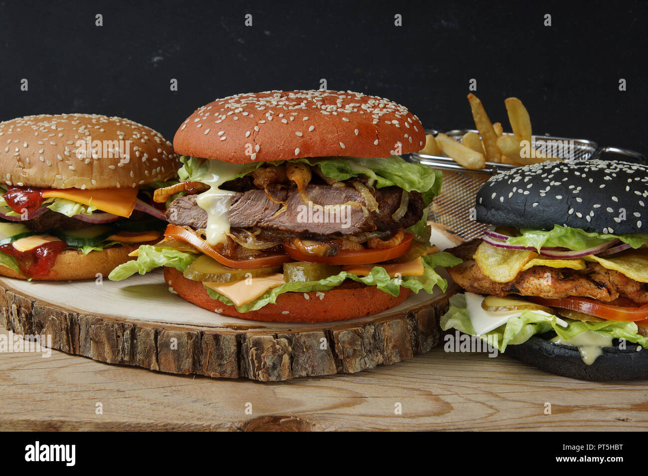Three large beautiful burger with buns of different colors and different fillings, chicken, meat patty and steak. Stock Photo