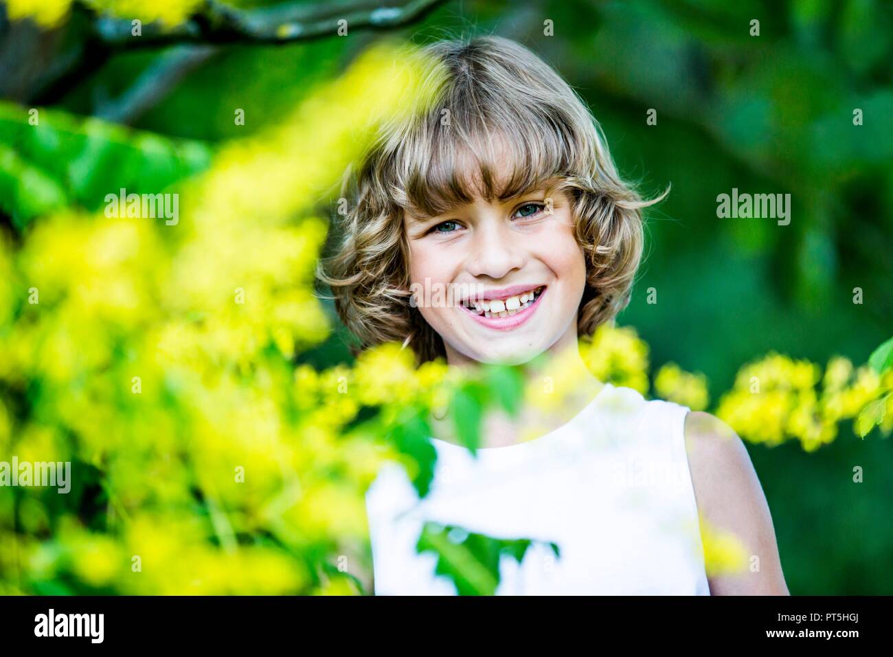 Portrait of young boy with yellow flowers in foreground, smiling. Stock Photo