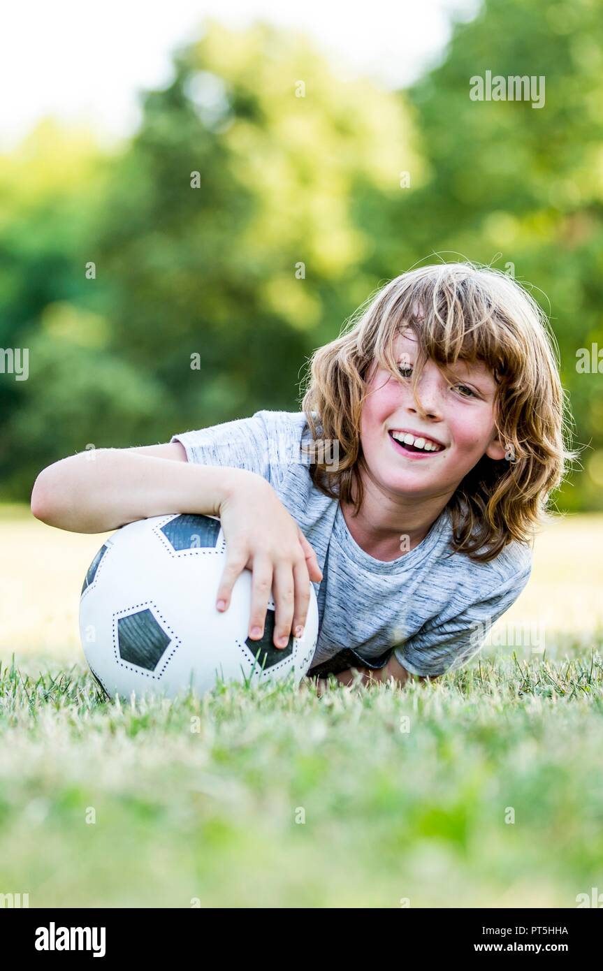 Boy holding football while lying in park, smiling, portrait. Stock Photo
