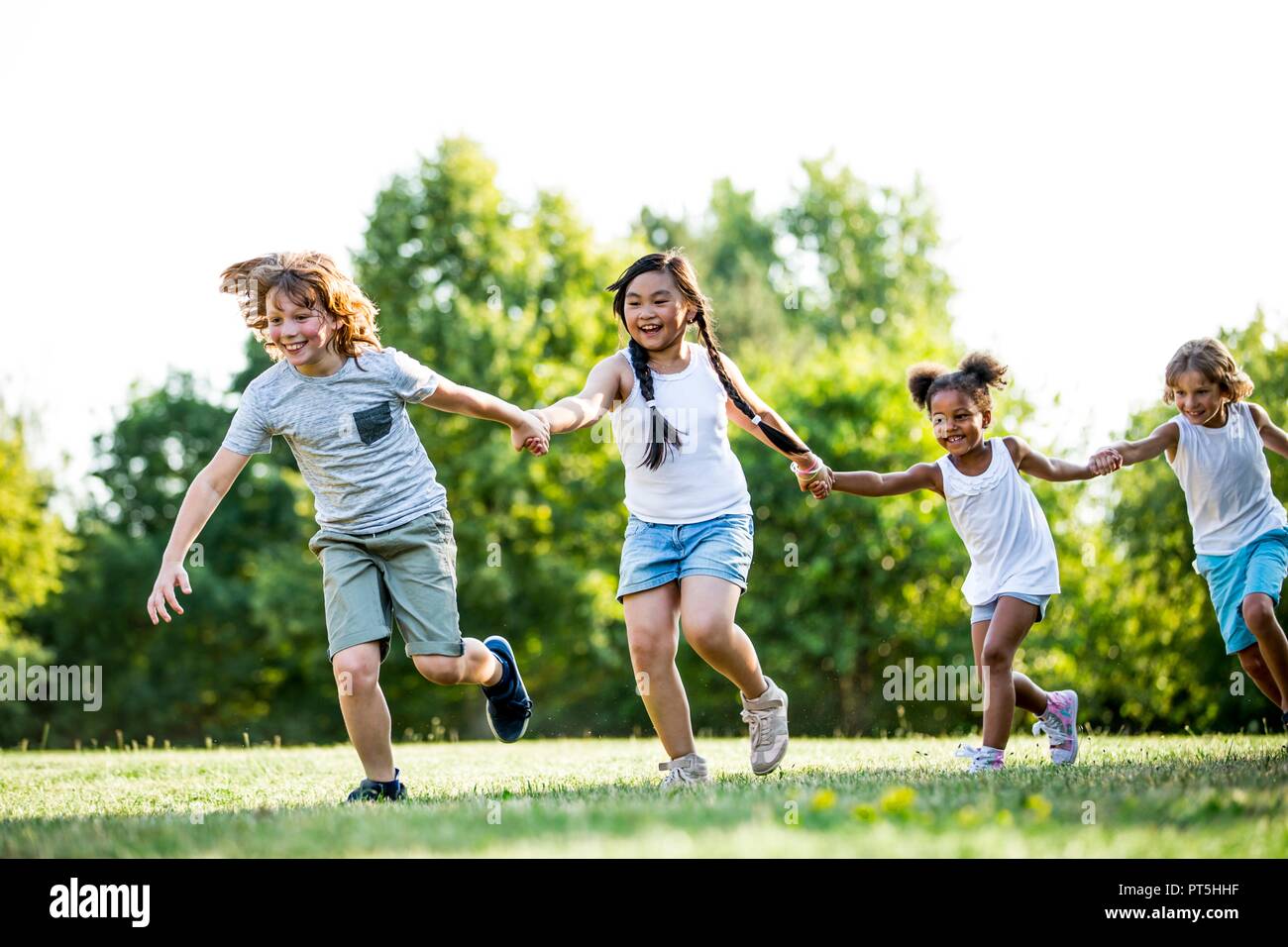 Children holding hands and running in park, laughing. Stock Photo