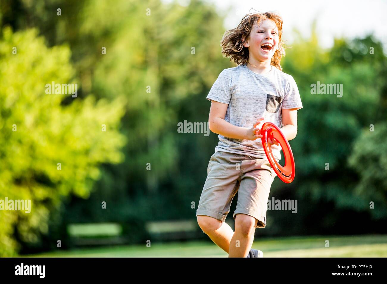 Boy playing with flying disc in park, laughing. Stock Photo