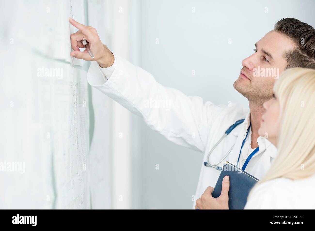 Portrait of mature male and female doctors inspecting white board. Stock Photo