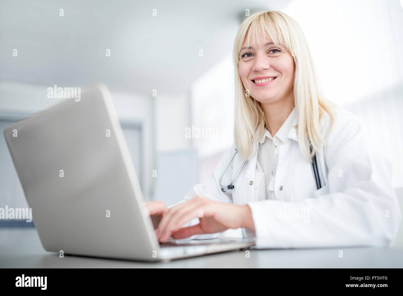 Female doctor using laptop and smiling. Stock Photo