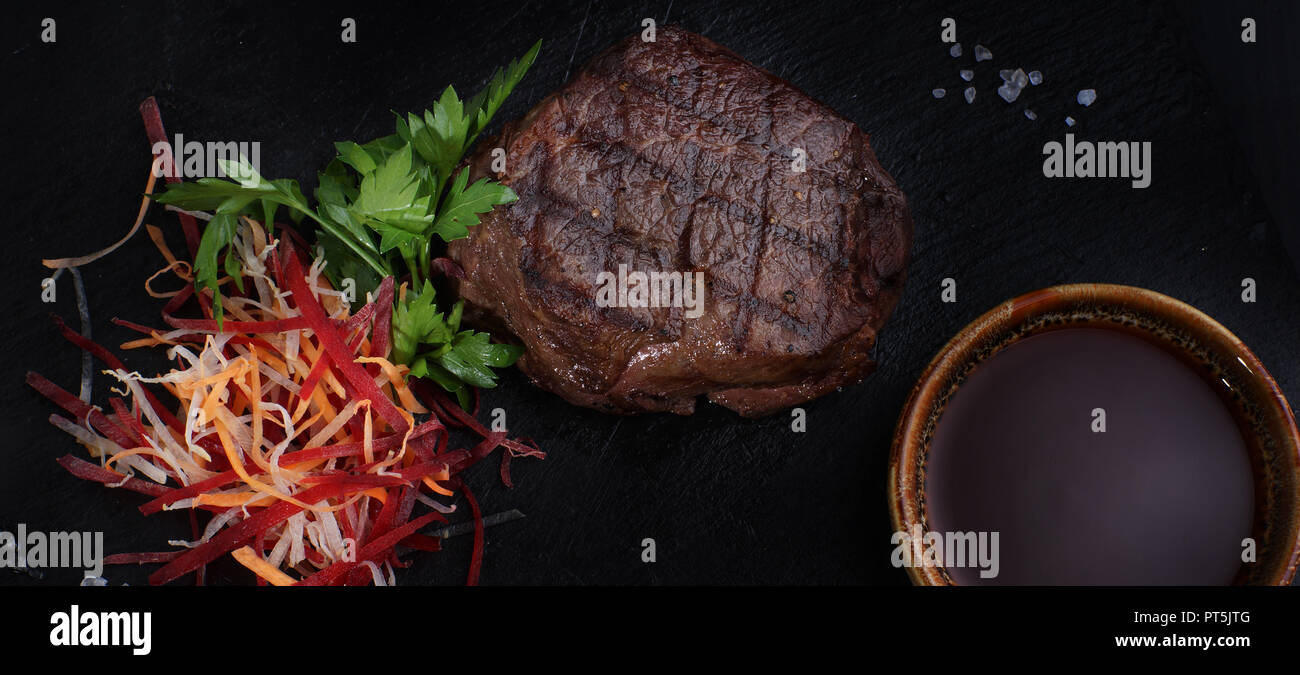 Beef medallion steak with vegetables and sauce on a black background