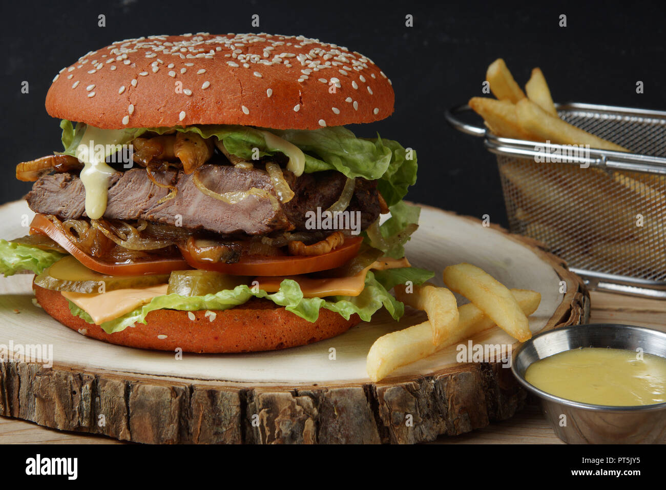 A large red burger with a piece of meat, tomatoes, pickled cucumbers, cheese, fried onion and lettuce, the sauce drains a large mouth-watering drop. Stock Photo