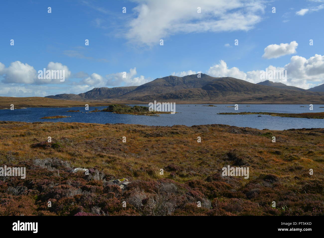 Scottish loch with heather on rocky and peaty ground with hills and blue cloudy sky in the background re scenery Isle of Harris Outer Hebrides UK Stock Photo