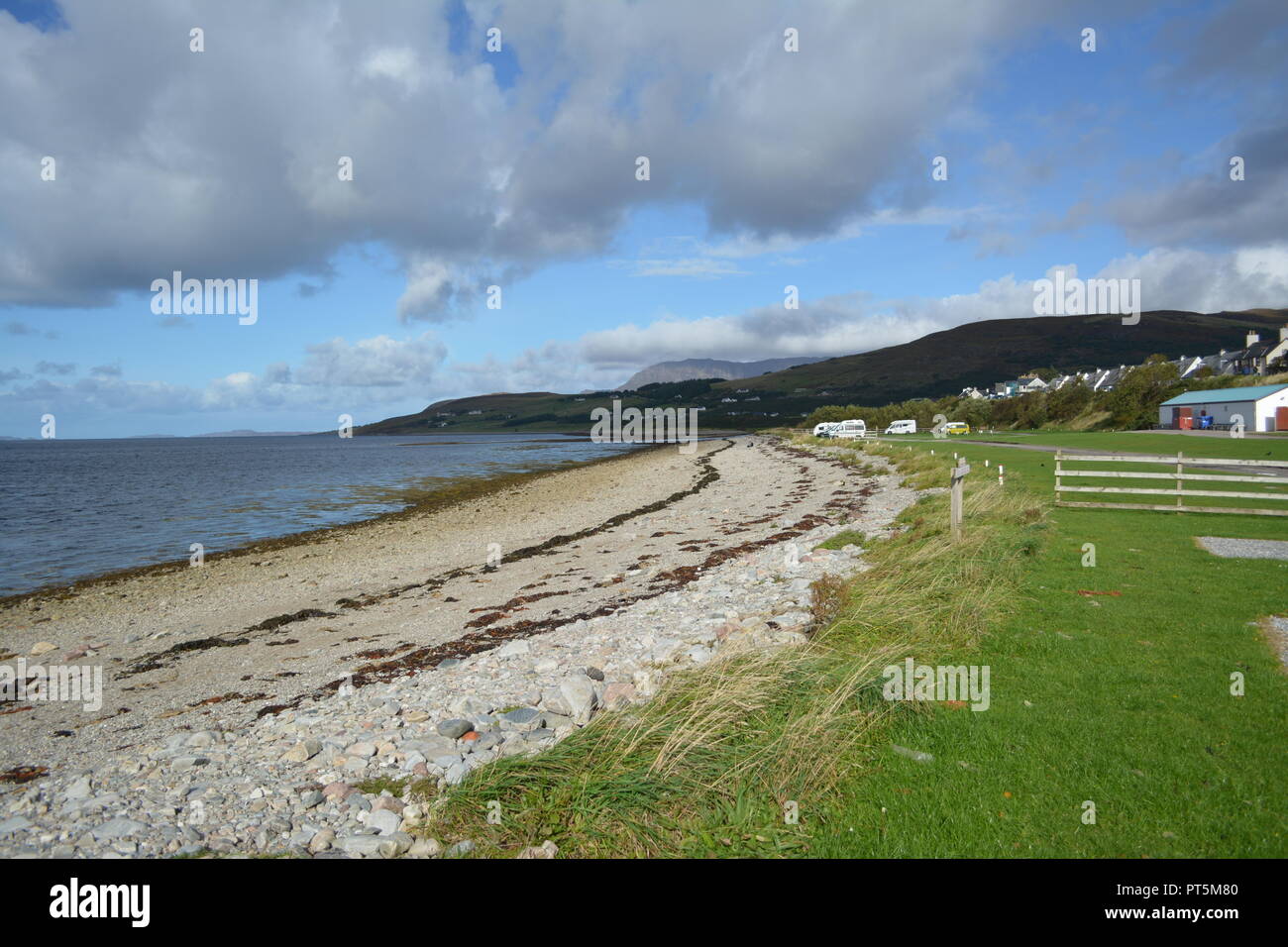 Deserted pebble beach strewn with seaweed fronting Broomhill camp caravan site Ullapool Scotland UK with sea blue sky and clouds in the background Stock Photo