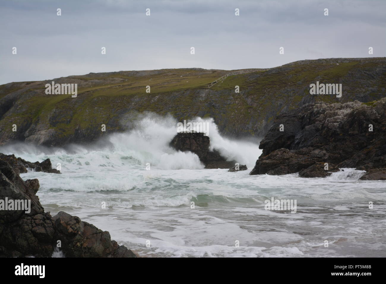 Waves crashing into the rocks close to the shoreline on a stormy and windy overcast and rainy autumn day with rocky coastline in the background UK Stock Photo