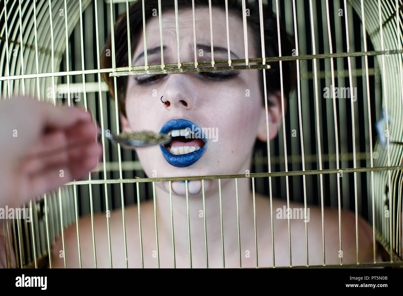 Conceptual shot of woman with blue lips and bird cage on head taking