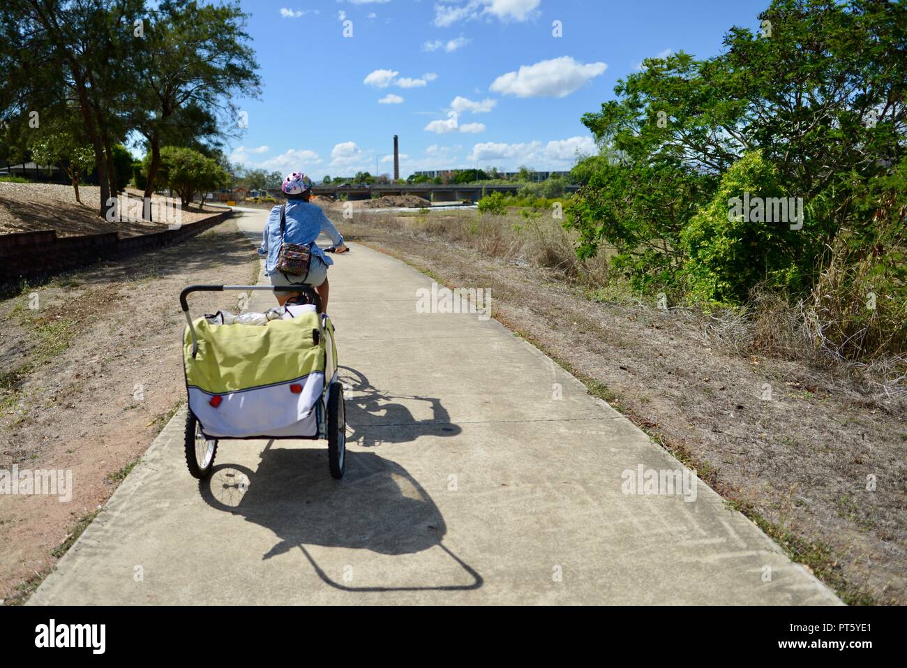 Woman riding a bicycle with a bicycle trailer for children, Townsville, QLD, Australia Stock Photo