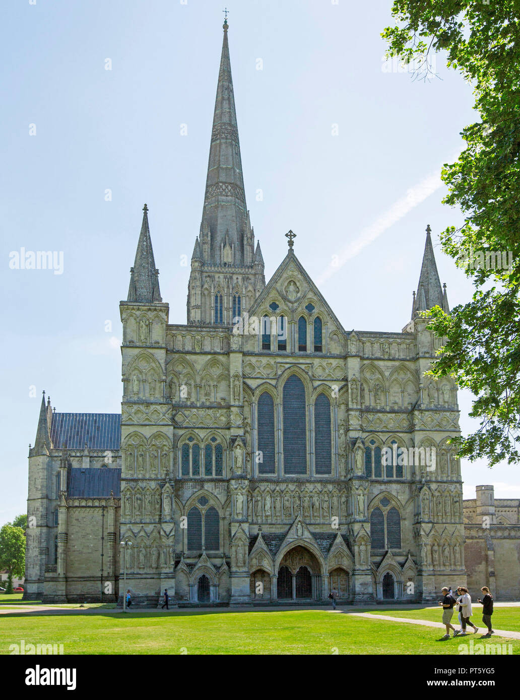 Ornate historic cathedral in Salisbury, Wiltshire England with people on lawns in foreground and spire reaching into blue sky Stock Photo