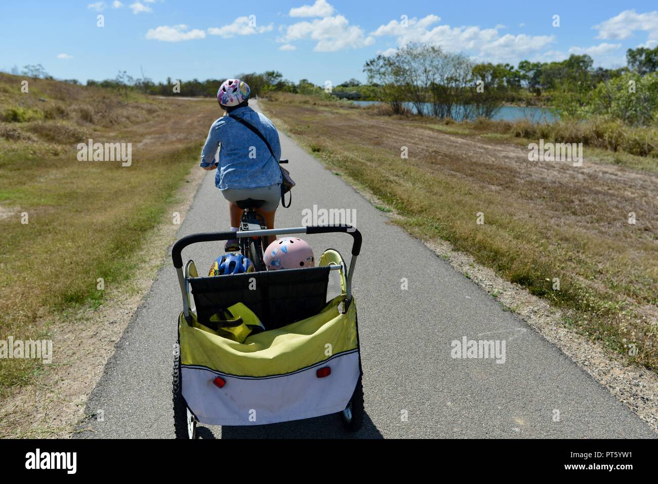 Woman riding a bicycle with a bicycle trailer for children, Townsville, QLD, Australia Stock Photo