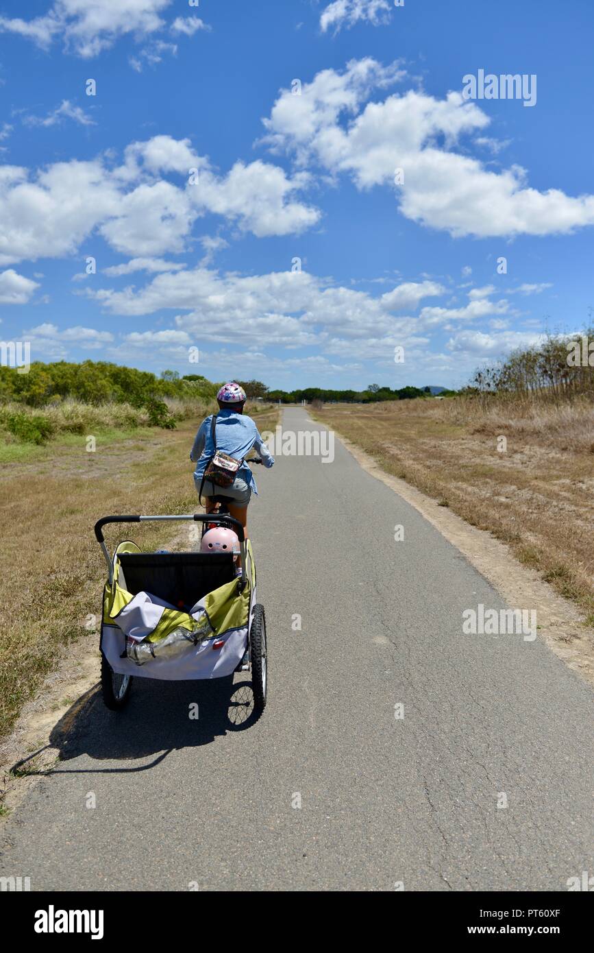 Woman riding a bicycle with a bicycle trailer for children, Townsville