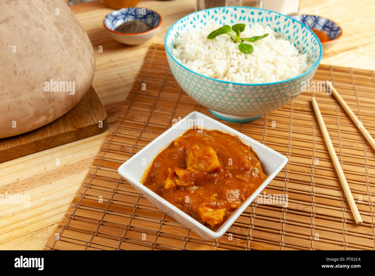 Portion of chinese chicken curry and a bowl of rice set out on a bamboo table mat with chopsticks Stock Photo