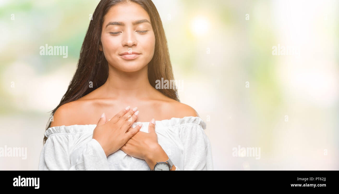 Young beautiful arab woman over isolated background smiling with hands on chest with closed eyes and grateful gesture on face. Health concept. Stock Photo