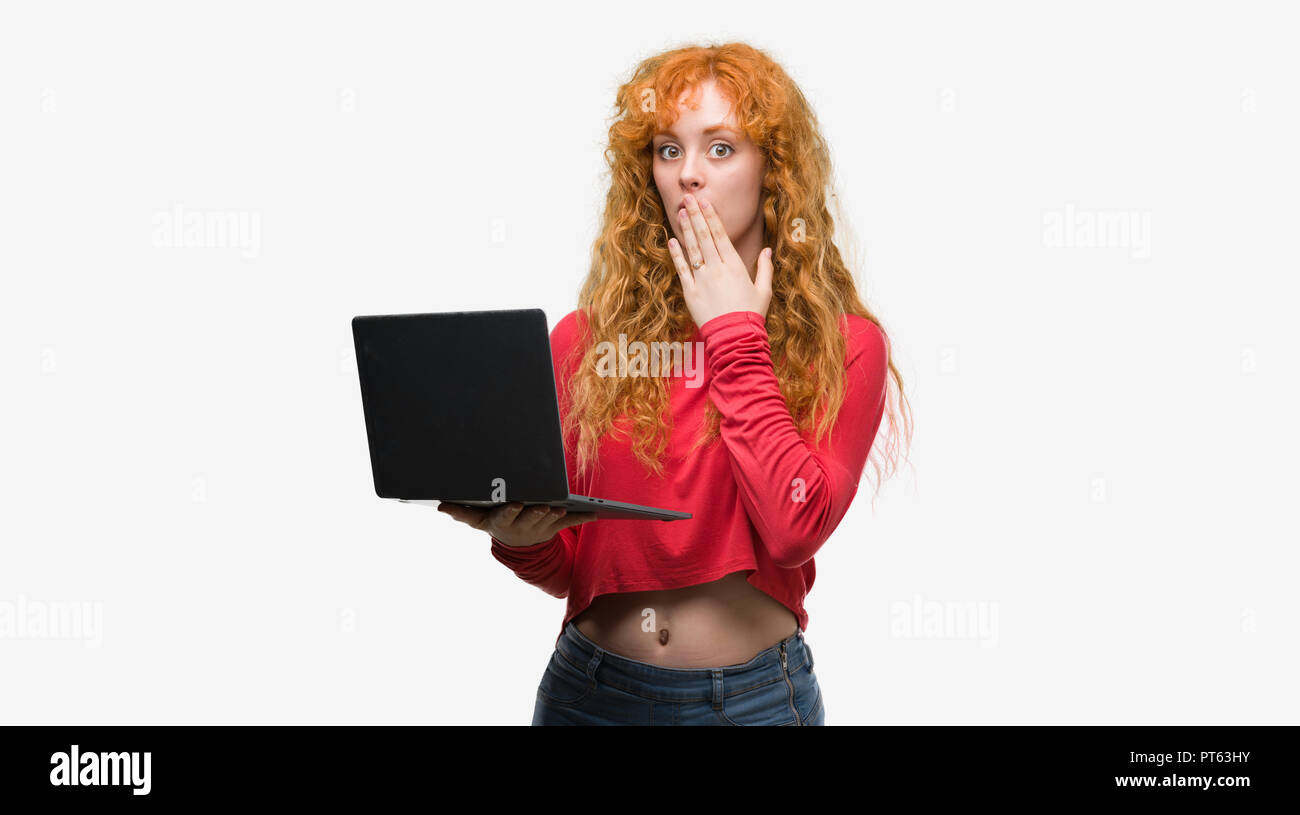 Young redhead woman using computer laptop cover mouth with hand shocked with shame for mistake, expression of fear, scared in silence, secret concept Stock Photo