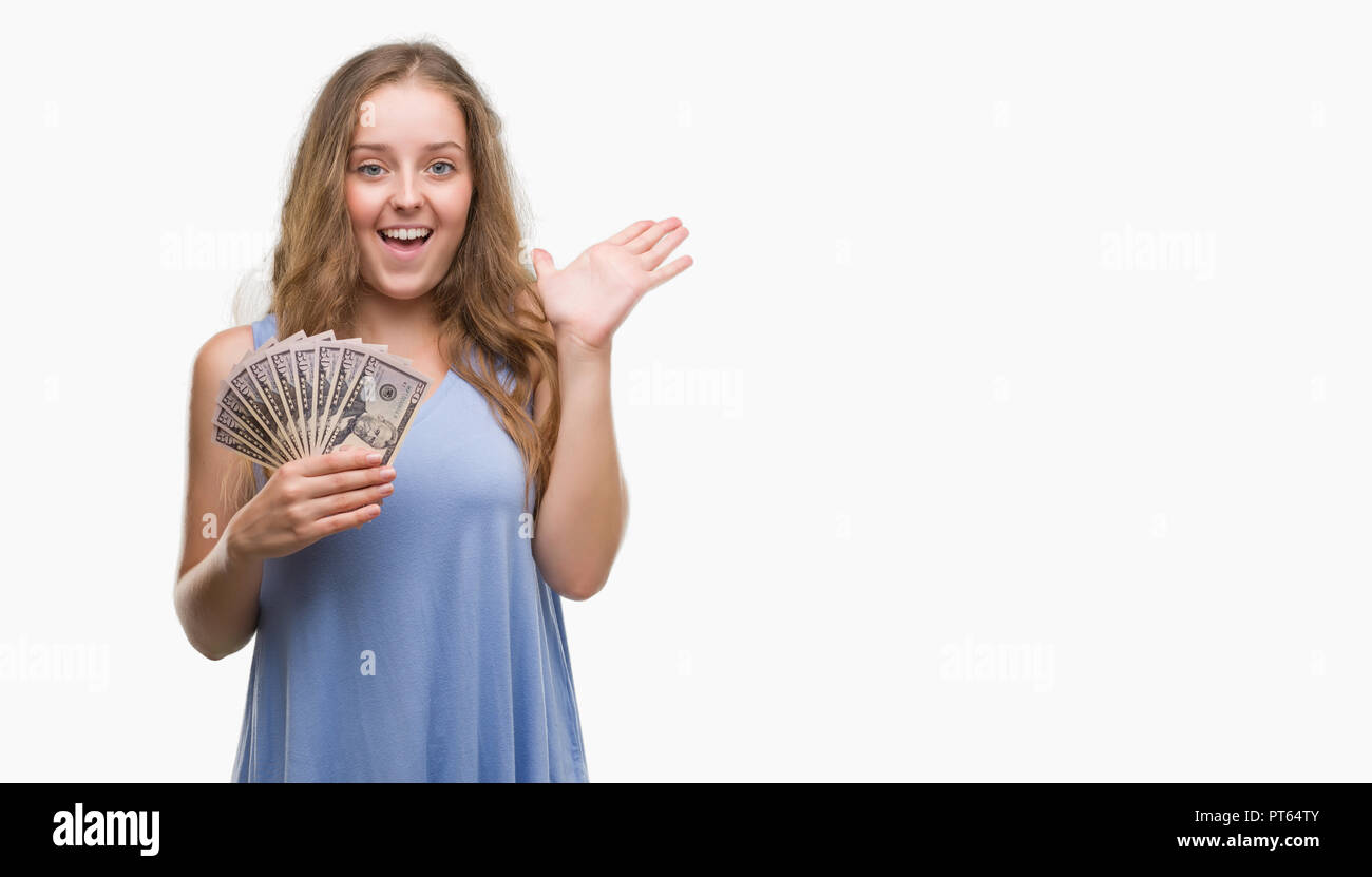Young blonde woman holding dollars very happy and excited, winner expression celebrating victory screaming with big smile and raised hands Stock Photo