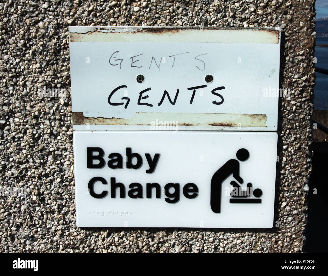 An amusing sign outside a public toilet begs the question; is the changing for the baby or the gent? Stock Photo