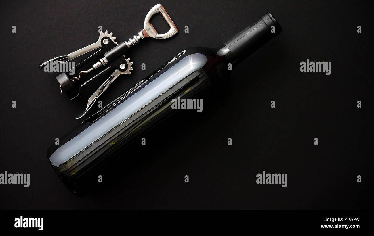 Red wine bottle and corkscrew on black matte background. Stock Photo