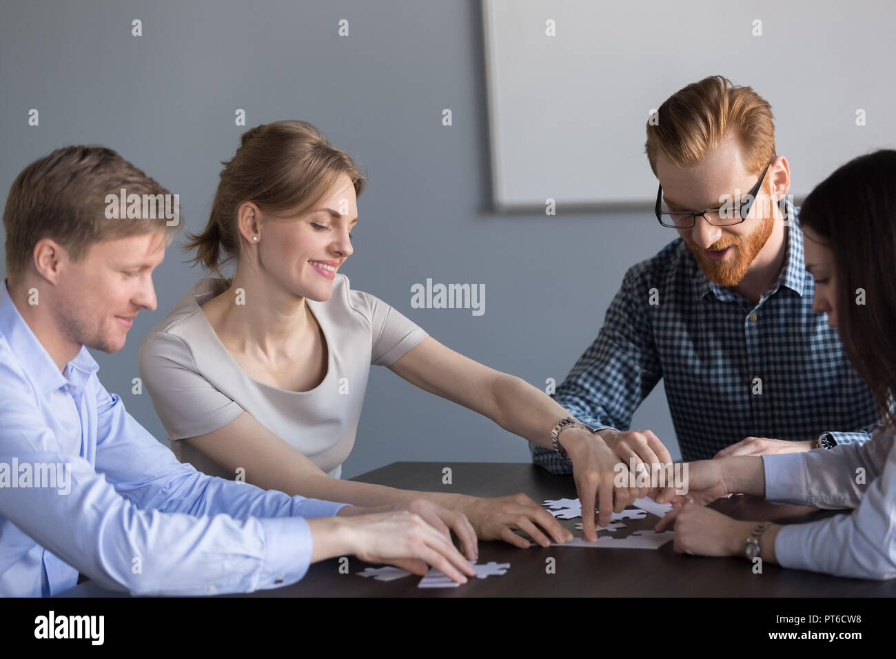 Smiling office team assembling puzzle together at meeting, teamb Stock Photo